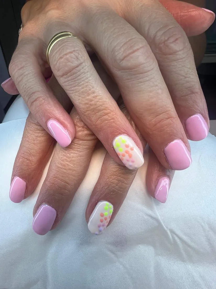 Manicura en rosa con una uña blanca decorada con puntos de colores, trabajo de Estética Vintage Spa